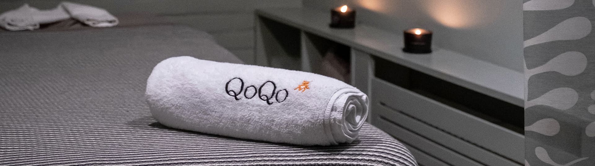 Een opgerolde handdoek met het QoQo-logo op een opgemaakte behandeltafel.