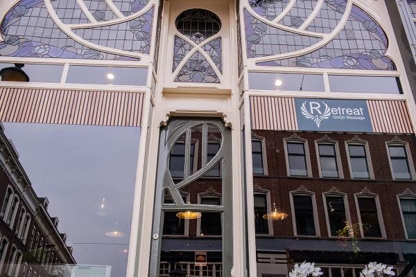 Glas-in-loodramen in de gevel met het bord van Retreat QoQo Massage.